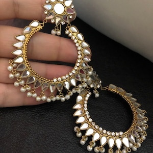 May include: Gold tone hoop earrings with a mirrored design and pearl accents. The earrings have a floral design at the top.