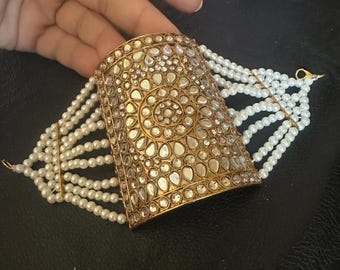 May include: A gold-toned bracelet with a decorative, ornate design featuring white stones. The bracelet is accented with a row of white pearls.