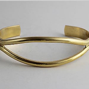 May include: A gold-toned metal bracelet with a curved, open design. The bracelet is made of two bands of metal that are joined together at the ends.
