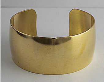 May include: A simple gold-colored metal cuff bracelet. The bracelet is smooth and has a rounded shape.