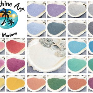 May include: A collection of twenty-four small piles of colored sand, each displayed inside a white seashell. The colors include various shades of blue, pink, purple, green, yellow, orange, and gray. A logo with the text Sunshine Art by Mariana is visible.