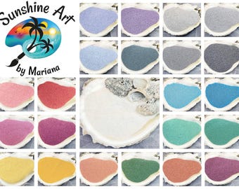 Pode incluir: Uma coleção de vinte e quatro pequenos montes de areia colorida, cada um apresentado dentro de uma concha branca. As cores incluem vários tons de azul, rosa, roxo, verde, amarelo, laranja e cinza. Um logotipo com o texto Sunshine Art by Mariana é visível.