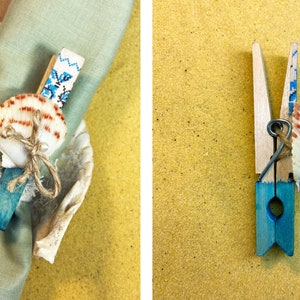 May include: A blue and white painted wooden clothespin with a seashell and twine bow. The clothespin is used as a napkin ring.