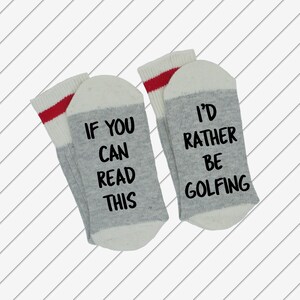 May include: A pair of grey and white socks with red stripes. One sock reads "If you can read this" and the other sock reads "I'd rather be golfing".