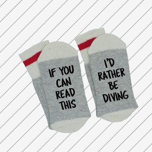 May include: A pair of grey and white socks with red stripes. One sock says "If you can read this" and the other sock says "I'd rather be diving".
