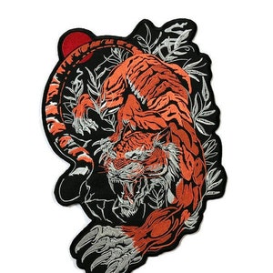 May include: An embroidered iron-on patch featuring a detailed orange and white tiger with a red sun behind it. The tiger is surrounded by black and white foliage.