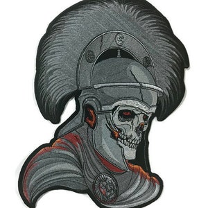 Può includere: Toppa ricamata da stirare con un teschio che indossa un elmo romano con una piuma. Il teschio è dettagliato con accenti rossi e arancioni. L'elmo è argentato e presenta un design a testa di leone sul davanti.