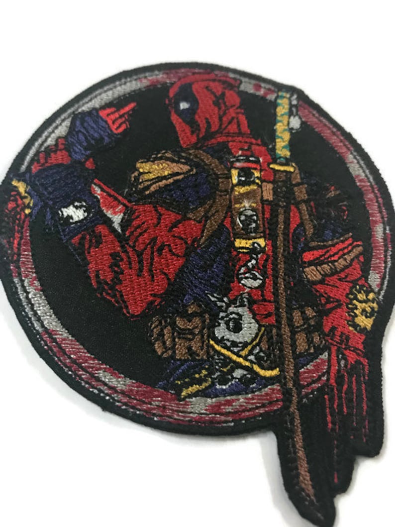 May include: Embroidered patch depicting Deadpool in a dynamic pose, set within a black circular frame. The patch showcases Deadpool's red and black costume, with a sword and intricate detailing. The design is vibrant and detailed.