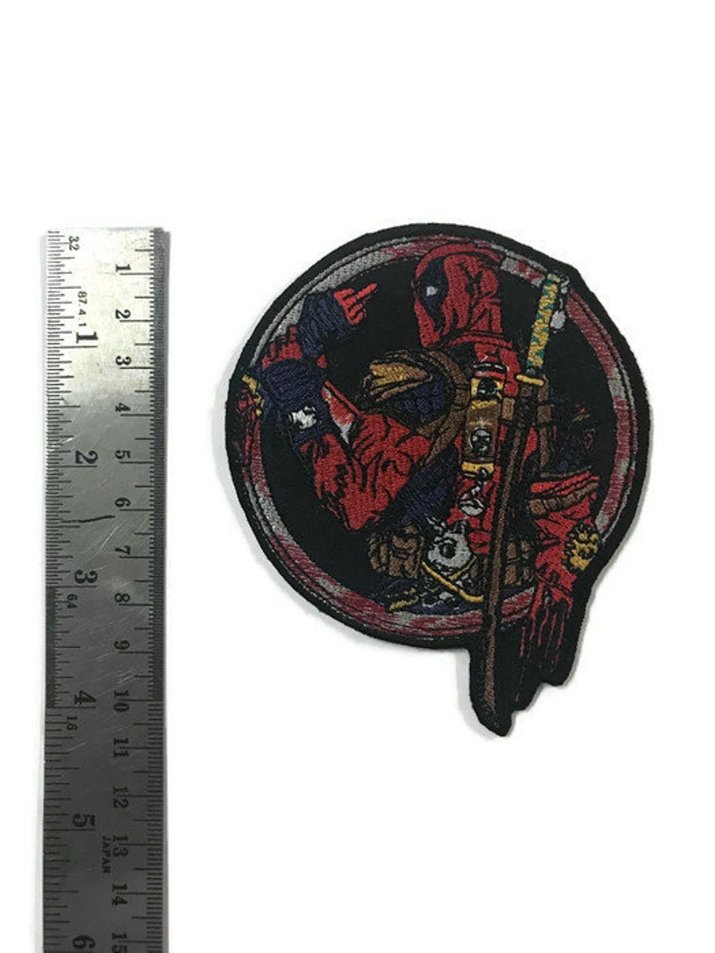 May include: Embroidered patch featuring Deadpool in a circular design. The patch is primarily red and black, with details of the character's costume and a sword. The patch measures approximately 7.6 cm in height.