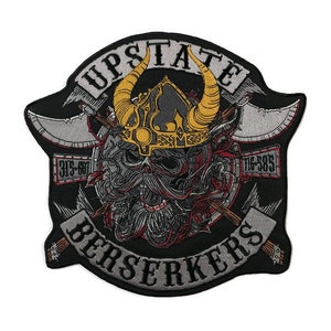 Pode incluir: Um remendo bordado preto e cinza com o texto "Upstate Berserkers" em um design de banner. O remendo apresenta uma caveira com chifres e barba, usando um capacete com uma coroa. A caveira é cercada por machados cruzados.