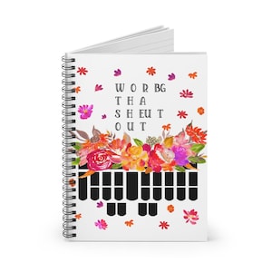 May include: A spiral-bound notebook with a white cover featuring the text "WOR BG THA SHEUT OUT" above a floral design in shades of pink, orange, and yellow. The bottom of the cover has a black and white pattern.
