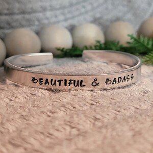 Puede incluir: Pulsera de plata con las palabras "Beautiful & Badass" grabadas.