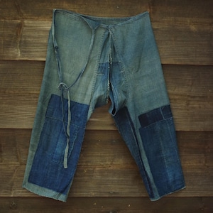 Può includere: Un paio di pantaloni in denim blu caratterizzati da un design patchwork con varie tonalità di indaco e azzurro. Il capo presenta una chiusura a laccio in vita e cuciture visibili, che mettono in risalto una struttura in tessuto testurizzato.