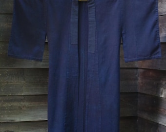 May include: A dark navy blue open-front jacket with wide, three-quarter length sleeves and a straight, structured collar. The garment features a simple, unadorned design with visible vertical stitching along the front panels and a solid, uniform color.