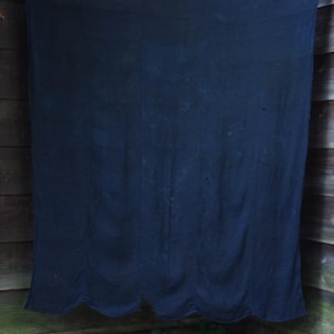 May include: A large, rectangular, dark navy blue fabric textile hanging from a thin, horizontal bamboo rod. The fabric features a scalloped bottom edge and a smooth, solid-coloured surface with subtle vertical folds throughout the material.