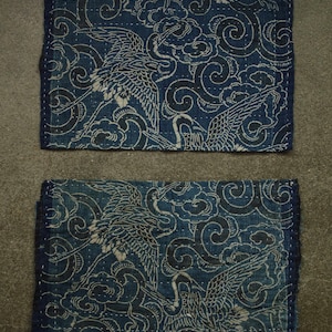May include: Two blue fabric squares with a white crane and cloud pattern. The fabric is quilted and has a distressed look.