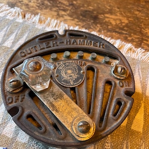 May include: Vintage Cutler-Hammer electrical switch with a clear glass handle and a metal plate. The switch is marked "OFF" and "ON" and has the text "VITA-MOTOR" and "PATENT PENDING". The switch is made of metal and has a circular shape.