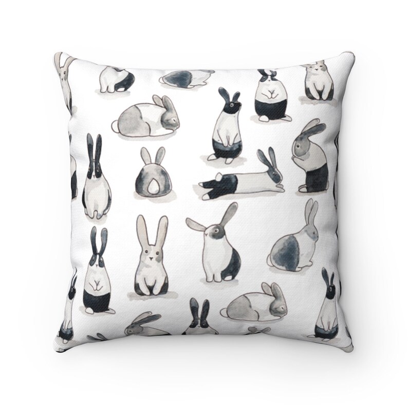 May include: A white throw pillow with a repeating pattern of black and white rabbits in various poses. The rabbits are drawn in a watercolor style.