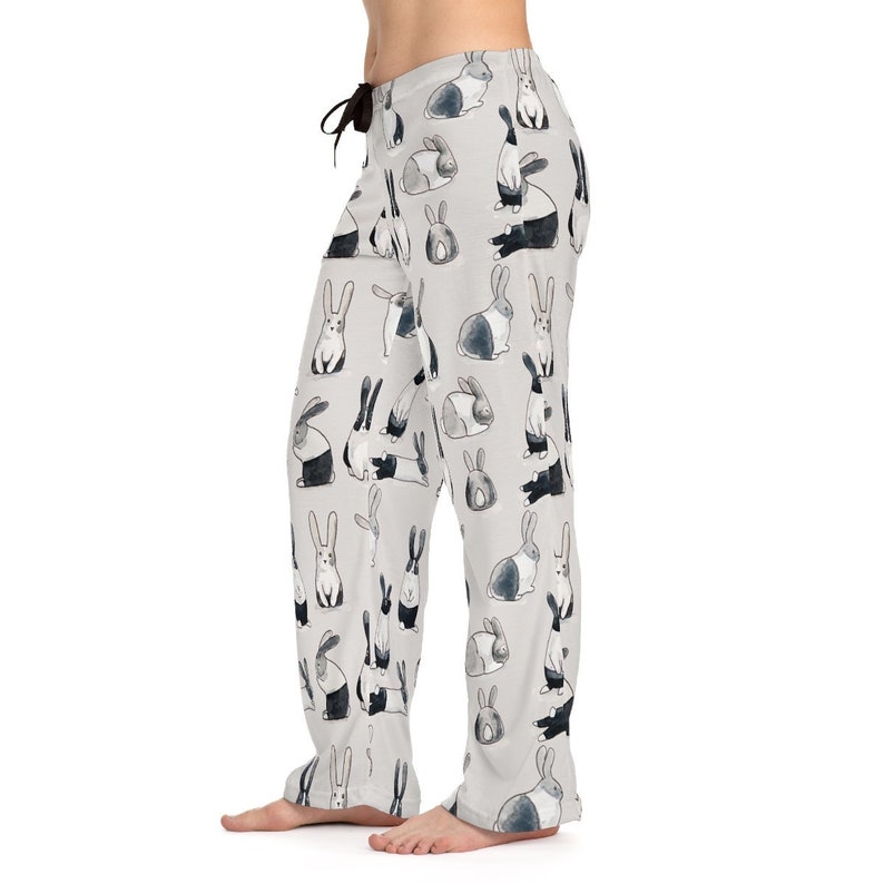Puede incluir: Pantal&oacute;n de pijama gris con un patr&oacute;n repetido de conejos negros y blancos. Los conejos est&aacute;n en varias poses, incluyendo sentados, de pie y saltando.