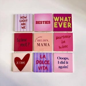 Könnte beinhalten: Neun quadratische dekorative Fliesen mit verschiedenen Phrasen in verschiedenen Farben. Zu den Phrasen gehören "How lucky are we", "Besties", "Whatever", "Wine not?", "Partner in wine" und "Oops, I did it again!"