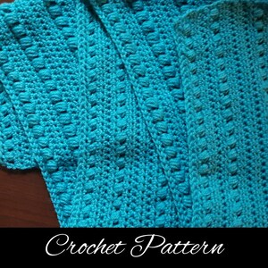May include: A close-up of a turquoise crochet pattern with a textured stitch. The pattern is made with a single crochet stitch and a bobble stitch. The pattern is repeated throughout the fabric.
