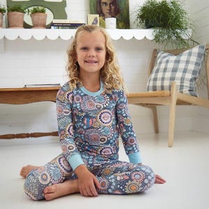 May include: A child wearing a two-piece pajama set. The long-sleeved top and pants are patterned with a floral design in shades of blue, pink, and orange. The pajamas have light blue cuffs and a light blue neckline.