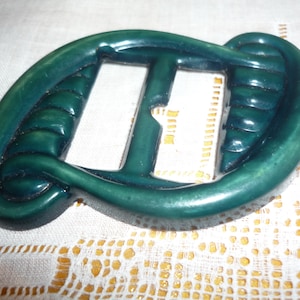 Peut inclure: Une boucle en plastique vert foncé avec un design unique. La boucle a une finition lisse et brillante et une forme légèrement incurvée.