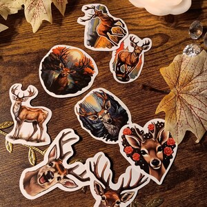 May include: Set of 7 deer stickers with various designs. The stickers feature a variety of deer in different poses, including a deer with antlers, a deer with a heart, and a deer with a flower crown. The stickers are all on a white background.