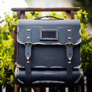 May include: A dark blue metal mailbox with a distressed finish and gold accents. The mailbox has a rectangular opening with a black metal flap and a handle on the top.