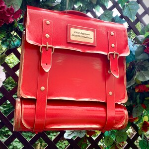 May include: A red metal mailbox with a brass nameplate that reads "PACE Angelina et GRAVELIN Guillaume". The mailbox has a rolled top and two straps with brass buckles.