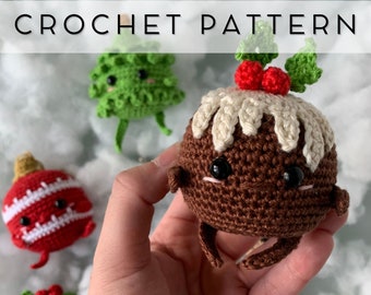 May include: A hand holds a crocheted Christmas pudding with a cream-colored top, red berries, and green leaves. Other crocheted Christmas ornaments, including a tree and a red bauble, are in the background. The text "CROCHET PATTERN" is at the top.