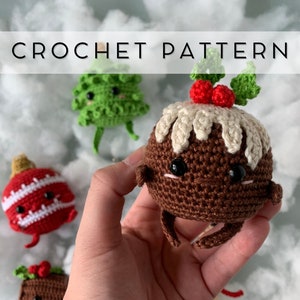 May include: A crocheted Christmas pudding with a cream-colored top, red berries, and green leaves is held in a hand. Other crocheted Christmas ornaments, including a tree and a red ornament, are in the background. The text "CROCHET PATTERN" is at the top.