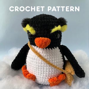 May include: A crocheted penguin toy with a black head and wings, a white body, and orange feet and beak. The penguin has yellow accents on its head and a tan satchel. The text "CROCHET PATTERN" is displayed above the penguin.