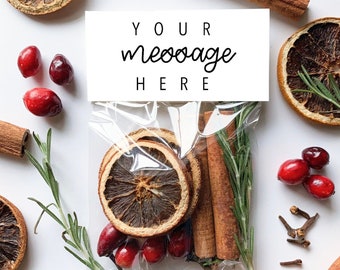 May include: A clear cellophane bag containing dried orange slices, cinnamon sticks, rosemary sprigs, and cranberries. The words "YOUR message HERE" are printed on a white label. The arrangement is surrounded by additional ingredients.