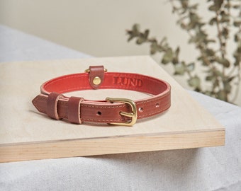 May include: A red leather dog collar with a brass buckle and the word "LUND" embossed on the collar.