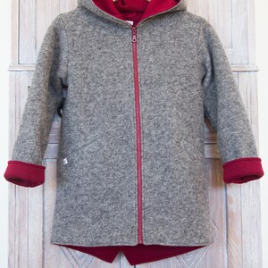 May include: A gray hooded jacket with a red zipper and red lining. The jacket has a hood and long sleeves.