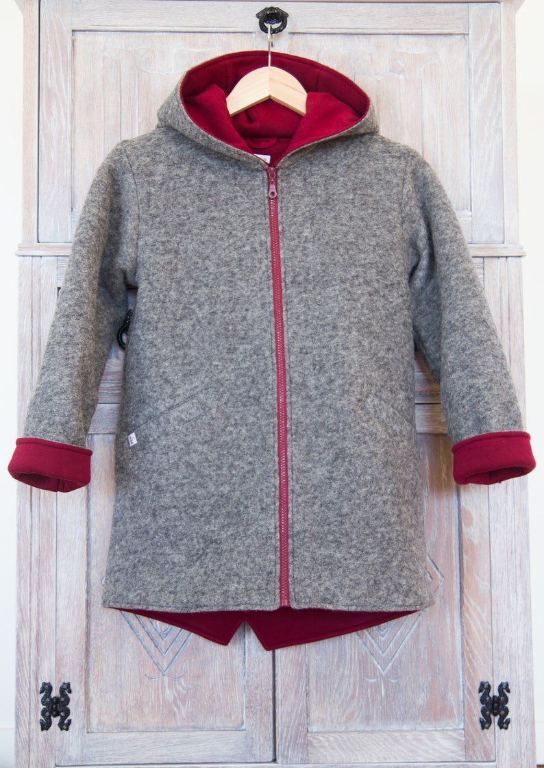 May include: A gray hooded jacket with a red zipper and red lining. The jacket has a hood and long sleeves.