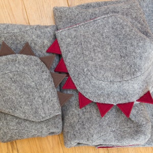 May include: Two gray felt dinosaur costumes with red and brown felt accents. The costumes have a hood with a pointed shape and a tail.