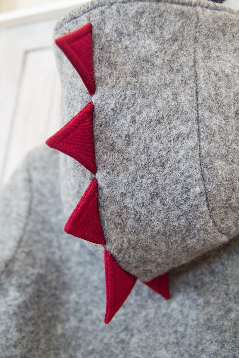 May include: Gray hooded sweatshirt with a red felt dinosaur tail. The tail is made of several triangular shapes.