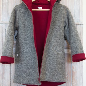 May include: A gray hooded jacket with a red lining. The jacket is unzipped and hanging on a hanger. The jacket has a zipper closure and long sleeves.