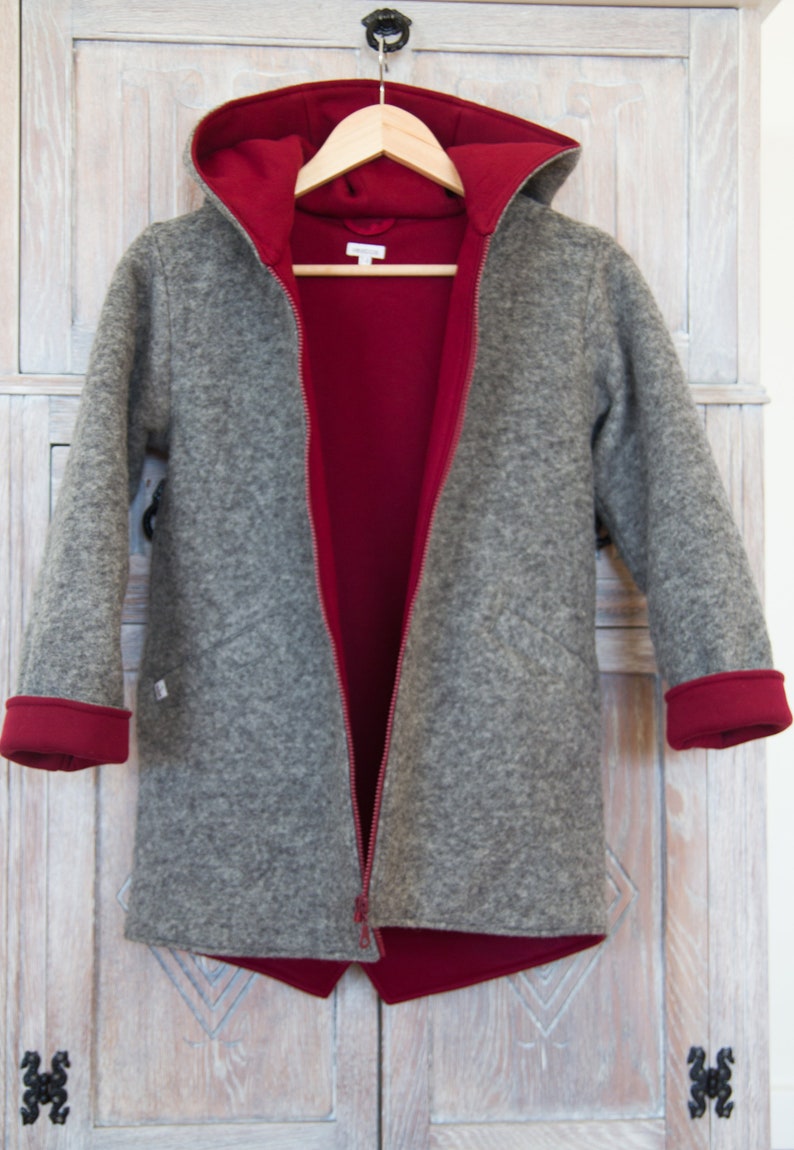 May include: A gray hooded jacket with a red lining. The jacket is unzipped and hanging on a hanger. The jacket has a zipper closure and long sleeves.