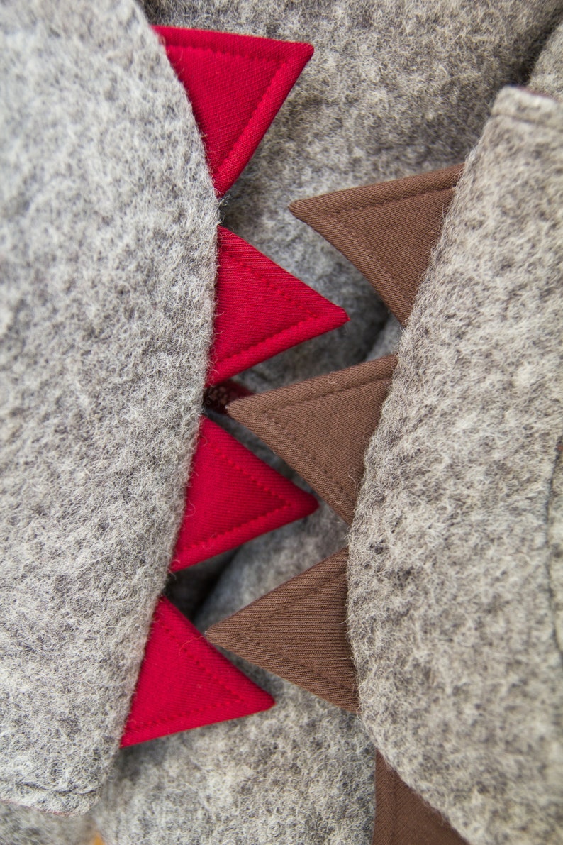 May include: A gray hooded sweatshirt with red and brown triangular patches sewn on the back. The patches are arranged in a row, with the red patches on the left and the brown patches on the right.