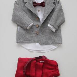 Puede incluir: Una chaqueta de lino gris con botones de madera, una camisa de lino blanca con una pajarita burdeos y un pantal&oacute;n de lino rojo con lunares blancos.