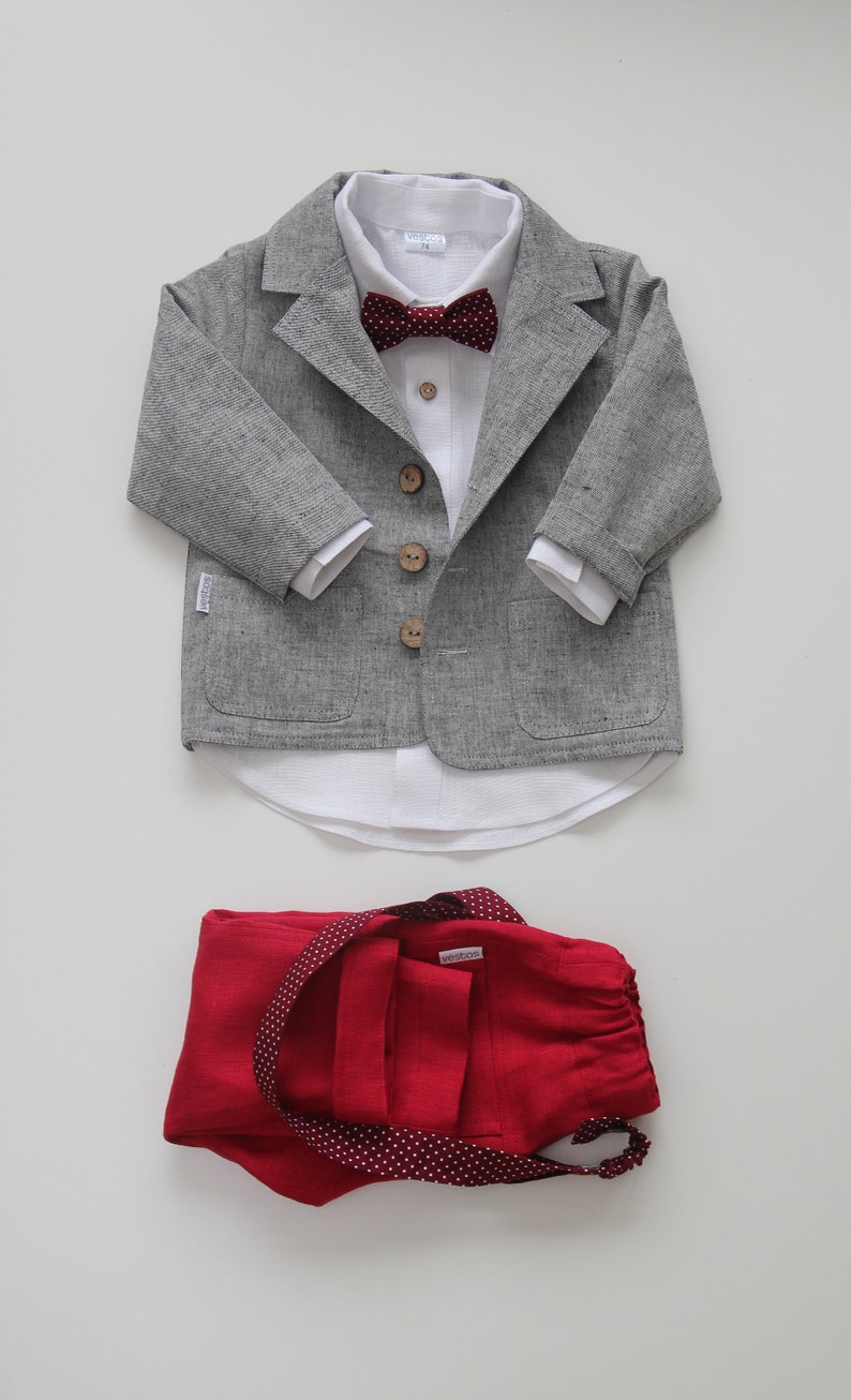 Puede incluir: Una chaqueta de lino gris con botones de madera, una camisa de lino blanca con una pajarita burdeos y un pantal&oacute;n de lino rojo con lunares blancos.