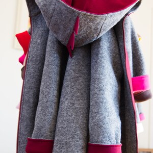 May include: A gray hooded jacket with a red lining and red trim. The jacket has a zipper closure and is hanging on a hanger.