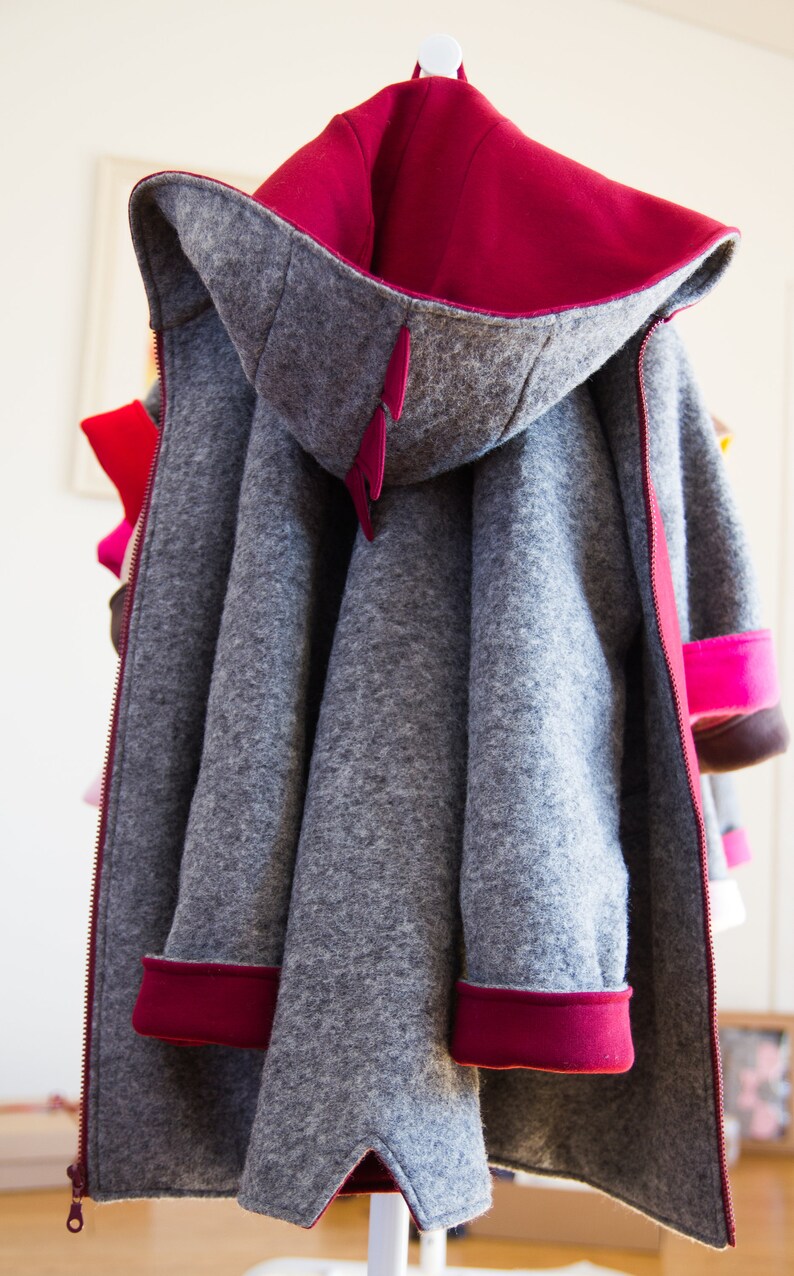 May include: A gray hooded jacket with a red lining and red trim. The jacket has a zipper closure and is hanging on a hanger.