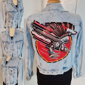 May include: Light blue denim jacket with a large "Screaming for Vengeance" Judas Priest album cover patch on the back. The jacket has silver studs around the patch and along the bottom hem.