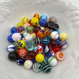 May include: A collection of assorted glass marbles in a variety of colours and patterns, including solid, translucent, and opaque spheres with stripes, swirls, and polka dots, clustered together in a pile with diverse textures and finishes.