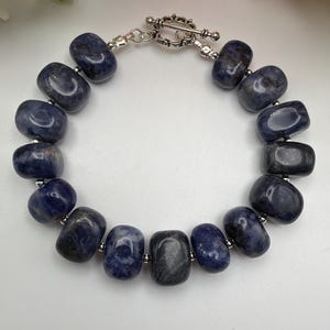 Peut inclure: Un bracelet composé de pierres arrondies bleu foncé. Les pierres sont enfilées avec un fermoir argenté. Un bijou simple et élégant.