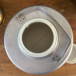 May include: A silver metal beverage cooler with a white lid and a handle. The cooler has a textured surface and a round opening.